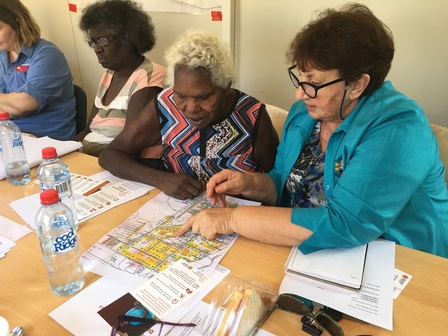 An Aboriginal lady and a caucasian lady look at a map of housing lots at a community meeting